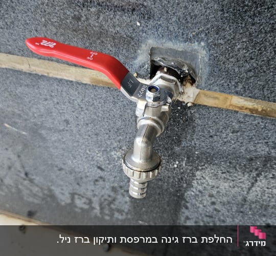 ברז מתכת עם ידית אדומה על קיר אפור